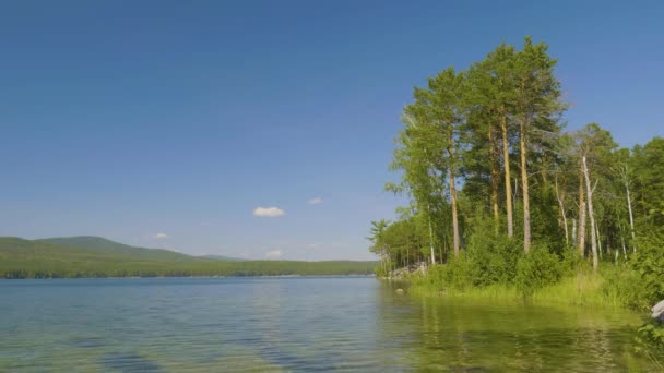 Gyönyörű kék tiszta víz a tó partján. Erdős táj tükröződik a víz partján — Stock videók