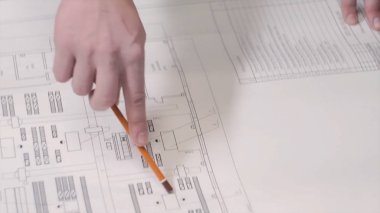 Bir adam bir çizim veya planı tablosundaki bir kalem kullanarak gösterir. Adam masada inşaat planları göster. İş adamı mimar ya da göstermek onların çalışma mimari modeli ofiste.