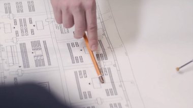Bir adam bir çizim veya planı tablosundaki bir kalem kullanarak gösterir. Adam masada inşaat planları göster. İş adamı mimar ya da göstermek onların çalışma mimari modeli ofiste.