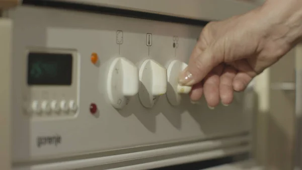 มือผู้หญิงเปิดเตาแก๊สในครัวสีขาว ผู้หญิงเปิดเตาในครัวใกล้ๆ — ภาพถ่ายสต็อก