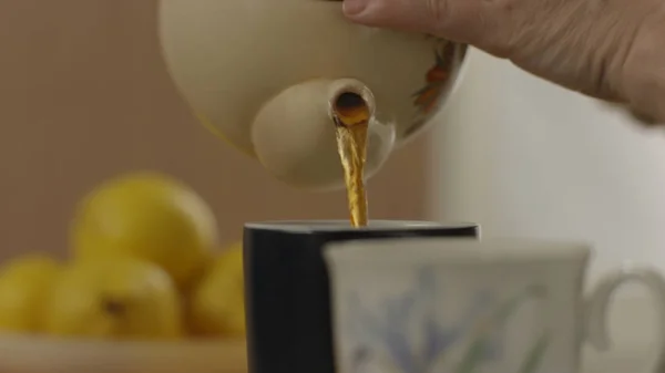 Womans hand pour tea from teapot into the glass