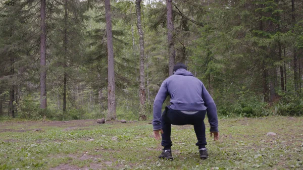 Un joven atlético saltando, realiza ejercicios de fuerza, un elemento crossfit. En el bosque de pinos, verano — Foto de Stock