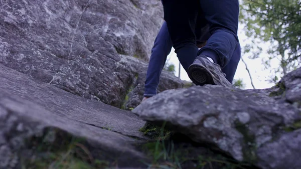 El hombre sube a una roca colgante cerca del bosque y se aferra. Atleta en las rocas en el bosque, estilo de vida activo — Foto de Stock