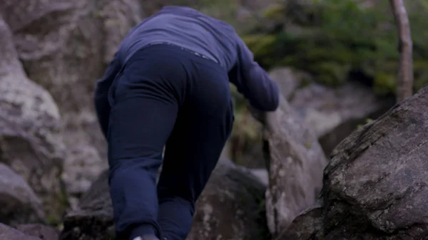 El hombre sube a una roca colgante cerca del bosque y se aferra. Atleta en las rocas en el bosque, estilo de vida activo — Foto de Stock