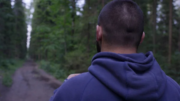 Hombre atlético con auriculares en la carretera a través del bosque. Hombre atlético de pie en el sendero a través del bosque de otoño. Vista trasera — Foto de Stock