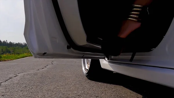 Nogi dziewczyny na sobie czarne buty na wysokim obcasie obserwuje się wydostać się z samochodu na ulicy — Zdjęcie stockowe