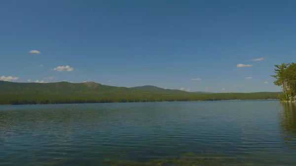Прекрасна блакитна чиста вода на березі озера. Лісовий пейзаж на узбережжі віддзеркалений у воді — стокове фото