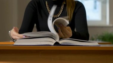 Kadın bir kitap aracılığıyla leafing eller. Kitap aracılığıyla leafing masada oturan kadın