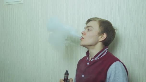 Young man vaping an electronic cigarette. Vaper hipster smoke vaporizer. Young man enjoying a satisfying e-cigarette standing in profile against white wall — Stock Video