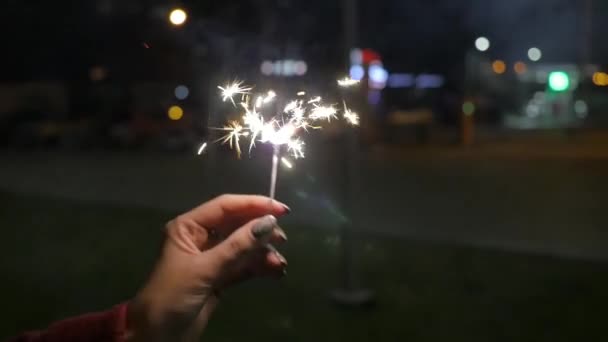 Close up van vrouw met sparkler op straat. Close-up van meisje met wonderkaarsen. Vrouwelijke hand hebt wonderkaarsen in de straat. Concept vakantie — Stockvideo