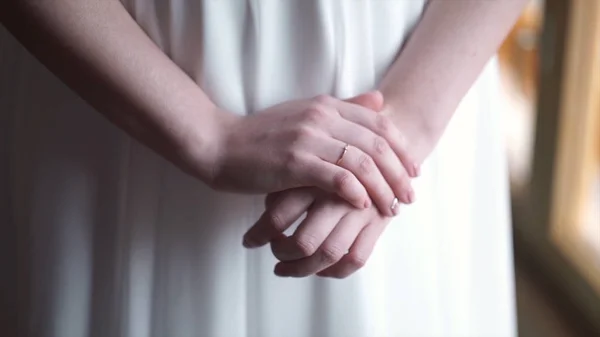 Mädchen in weißem Kleid steht am Fenster. Mädchen Hand mit Ehering oder Verlobungsring. schöne junge Frau in weißem Kleid bleibt zu Hause am Fenster. Morgen der Braut. — Stockfoto
