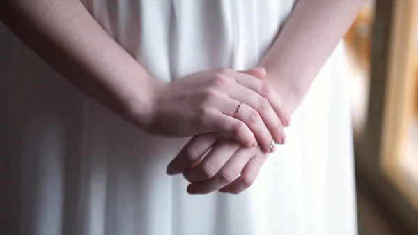 Girl in white dress staying near the window. Girls hand with wedding ring or engagement ring. Beautiful young woman in white dress stay near the window at home.Elegant. Morning of the bride. — Stock Photo, Image