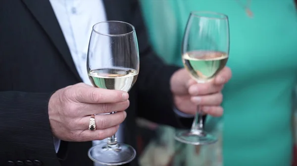 Gros plan de l'homme caucasien en costume noir et chemise blanche tenant deux grands verres avec du vin blanc. Gros plan de deux verres de champagne sur un plateau tenu par un beau garçon en smoking. Homme en costume tenant 2 — Photo