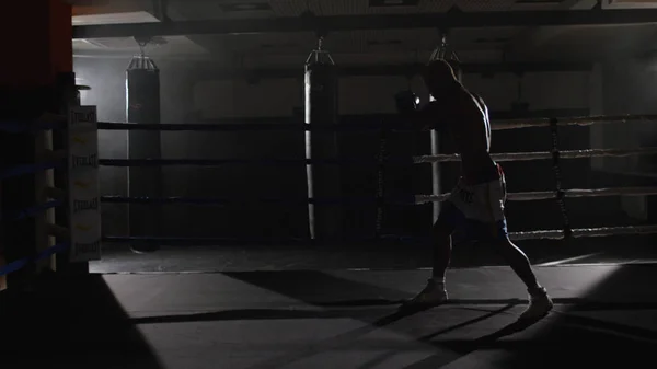 Kickbox pugilato ombra combattente sul ring. L'atleta combatte con la sua ombra. Giovane pugile in allenamento lanciando un pugno con bende sui pugni mentre si allena sul ring — Foto Stock