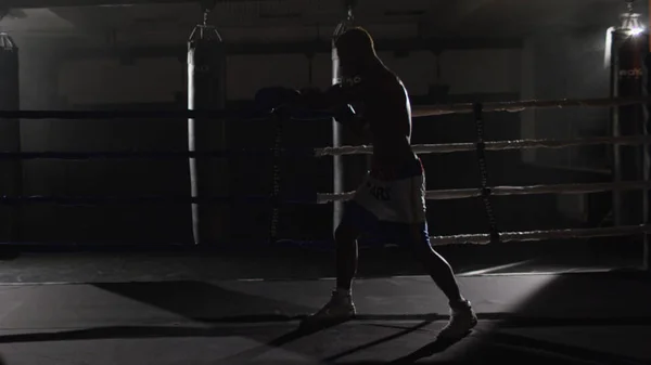 Kickbox pugilato ombra combattente sul ring. L'atleta combatte con la sua ombra. Giovane pugile in allenamento lanciando un pugno con bende sui pugni mentre si allena sul ring — Foto Stock