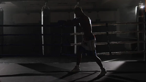 Kickbox-Kämpfer Schattenboxen im Ring. kämpft der Athlet mit seinem Schatten. junger Boxer im Training, der einen Schlag mit Bandagen auf die Fäuste wirft, während er im Ring trainiert — Stockfoto