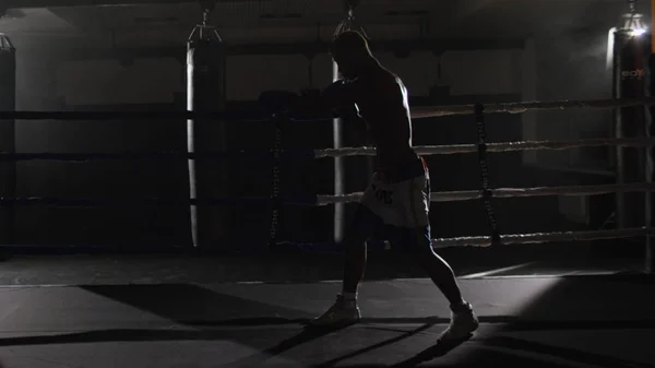 Kickbox boxeo sombra de combate en el ring. El atleta lucha con su sombra. Joven boxeador en entrenamiento lanzando un puñetazo con vendajes en sus puños mientras se ejercita en el ring —  Fotos de Stock