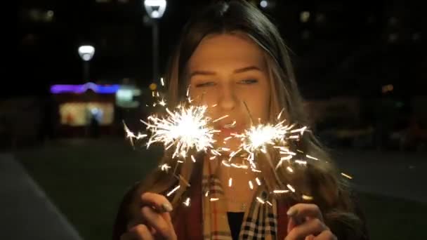 Jovem bela menina sorridente feliz segurando sparklers, posando na rua. Mulher com brilhos na rua. Conceito de férias — Vídeo de Stock