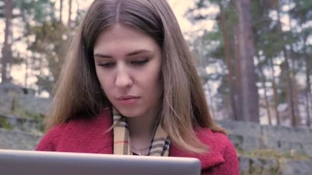 Młoda kobieta za pomocą tabletu w parku. Kobieta przy użyciu tabletu na zewnątrz na terenie parku. Młoda kobieta działa na tablecie w parku — Wideo stockowe