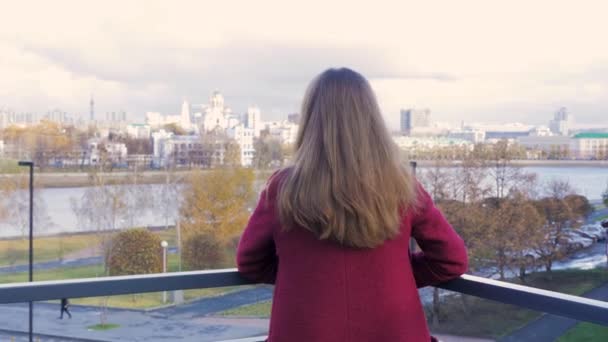 Vista trasera de la mujer de pie en el balcón y disfrutar de la vista de la ciudad. Vista posterior de la joven mujer de pie en el balcón — Vídeos de Stock