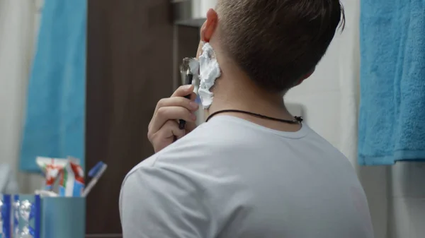 Young man with a disposable razor shaving his cheek close up. Guy shaving in the bathroom and cut himself. Scar — Stock Photo, Image