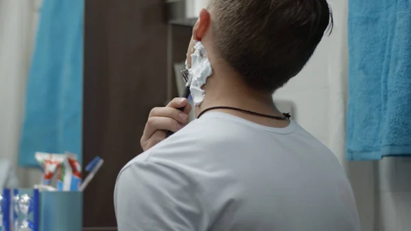 Young man with a disposable razor shaving his cheek close up. Guy shaving in the bathroom and cut himself. Scar — Stock Photo, Image