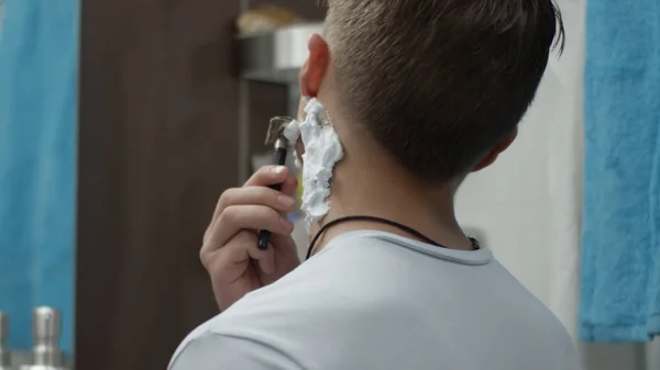 Young man with a disposable razor shaving his cheek close up. Guy shaving in the bathroom and cut himself. Scar — Stock Photo, Image