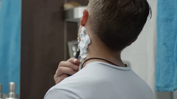 Молодой человек с одноразовой бритвой, бреющий щеку поближе. Парень бреется в ванной и порезался. Шрам — стоковое фото