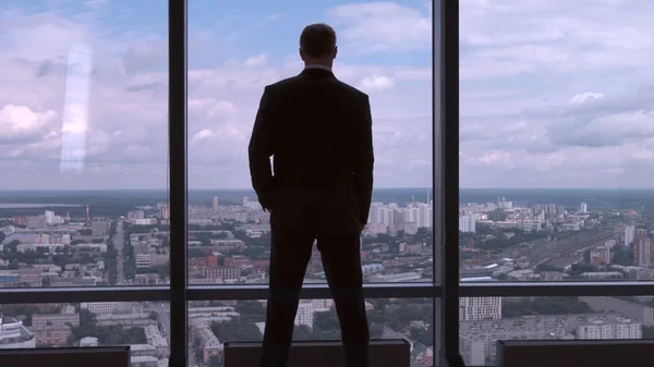 Full längd bakifrån av framgångsrik affärsman i kostym stående i kontor med händerna på midjan, VD. Affärsman från baksidan framför stadsutsikt på fönstret — Stockfoto