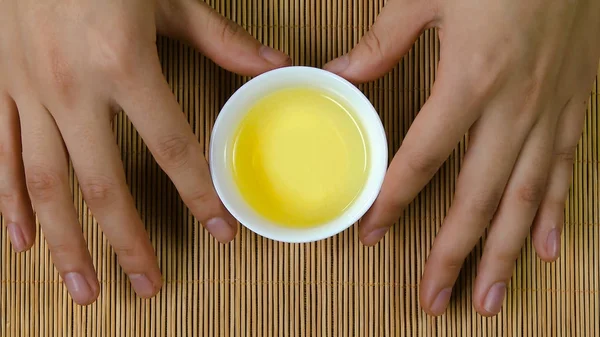 Femmes mains tenant tasse blanche de thé chinois fond de bambou, vue de dessus. Une femme tenant une tasse de thé. thé sencha japonais vert dans une tasse de fleurs — Photo