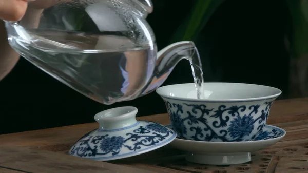 Processo di preparazione del tè, cerimonia del tè, tazza di tè nero appena preparato. Set da tè asiatico su tappetino di bambù, primo piano. Il cinese da una teiera lanciata — Foto Stock