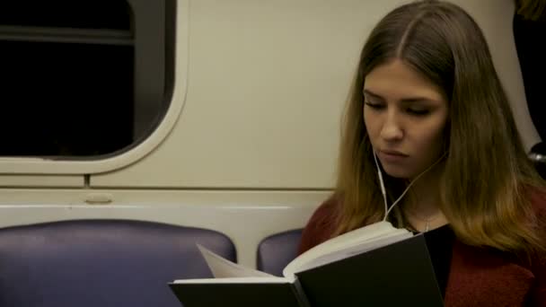 Junge schöne Frau sitzt in der U-Bahn und liest ein Buch - Pendler, Student, Wissenskonzept. junge Frau liest in der U-Bahn ein Buch — Stockvideo