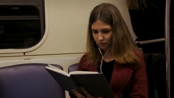 Mulher bonita jovem sentada no metrô lendo um livro - viajante, estudante, conceito de conhecimento. Jovem no metrô lendo um livro — Vídeo de Stock