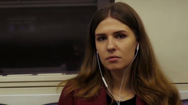 Wanita muda naik kereta bawah tanah dan mendengarkan musik di headphone. Wanita muda naik kereta metro, mendengarkan musik di headphone. Dengan musik di jalan — Stok Video