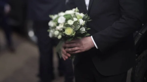 Bonito homem de negócios a segurar flores. Lustro em um terno que mantém um buquê de flores. Casamento boutonniere. Homem elegante vestido com um terno preto moderno e camisa branca segurando na mão um casamento flores — Fotografia de Stock