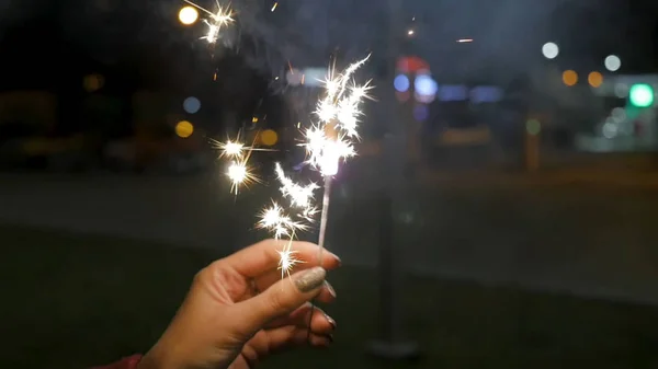 Female hand holding sparklers in the street. Close up of woman holding sparkler on the street. Closeup of Girl with Sparklers — Stock Photo, Image