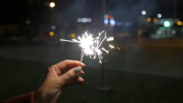 Female hand holding sparklers in the street. Close up of woman holding sparkler on the street. Closeup of Girl with Sparklers — Stock Photo, Image