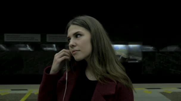 Ein junges Mädchen hört im U-Bahn-Tunnel über Kopfhörer Musik. Eine junge Studentin hört im U-Bahn-Tunnel mit großen Kopfhörern Musik. junge Frau hört Musik auf ihrem Smartphone an der — Stockvideo