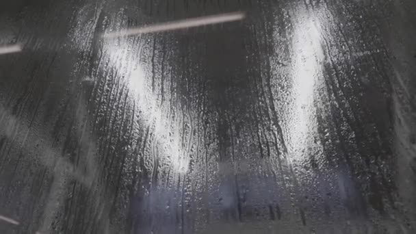 Капли воды на стекло. Капли дождя на черном стеклянном фоне. Природный образец дождевых капель. В городе идет дождь. Эффект от капли дождя сделать пар на окне — стоковое видео