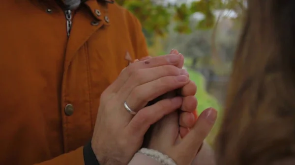 Un homme réchauffe les mains des femmes. Mariée et marié se tiennent la main et se réchauffent mutuellement dans un parc. Homme et femme se tenant la main. réchauffer les mains . — Photo