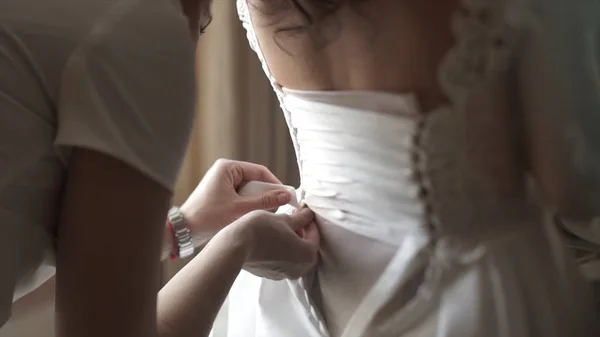 Κομψό όμορφες παράνυμφοι βοηθώντας πανέμορφη μελαχρινή νύφη σε λευκό φόρεμα Ετοιμαστείτε για το γάμο, πρωί παρασκευάσματα, γυναίκα, βάζοντας στο φόρεμα. Μαμα και φορέματα παράνυμφων, βοηθούν να ντύσουν ένα γαμήλιο φόρεμα — Φωτογραφία Αρχείου