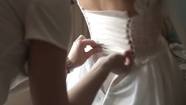 Eleganti belle damigelle d'onore che aiutano splendida sposa bruna in abito bianco prepararsi per il matrimonio, i preparativi del mattino, la donna che indossa il vestito. Mamma e damigella d'onore, aiutare a vestire un abito da sposa — Foto Stock