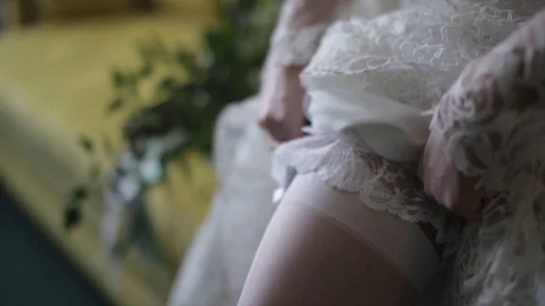 Sposa veste calze a piedi. Sposa di bellezza in un vestito che indossa calze da sposa all'interno. Ritratto femminile bella signora in un vestito. Primo piano delle mani della donna — Foto Stock