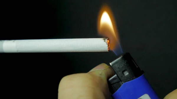 Mão iluminação mais leve cigarro closeup. Cigarro queimado no fundo preto. Cigarro closeup em fundo preto — Fotografia de Stock