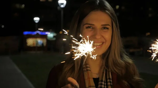 Jovem bela menina sorridente feliz segurando sparkler na rua. Conceito de férias. Menina com faíscas na rua — Fotografia de Stock
