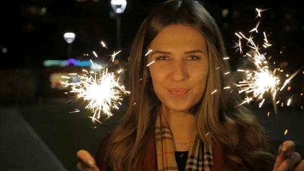 Jovem bela menina sorridente feliz segurando sparkler na rua. Conceito de férias. Menina com faíscas na rua — Fotografia de Stock