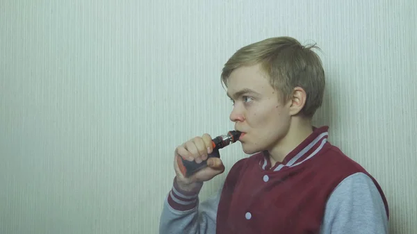 Young man vaping an electronic cigarette. Vaper hipster smoke vaporizer. Young man enjoying a satisfying e-cigarette standing in profile against white wall — Stock Photo, Image