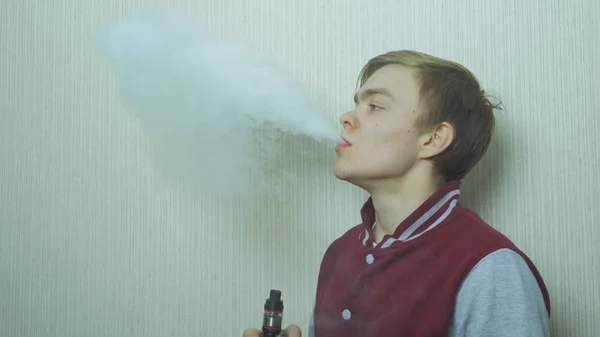 Un joven vapeando un cigarrillo electrónico. Vaporizador de humo Vaper hipster. Joven disfrutando de un satisfactorio cigarrillo electrónico de perfil contra la pared blanca — Foto de Stock