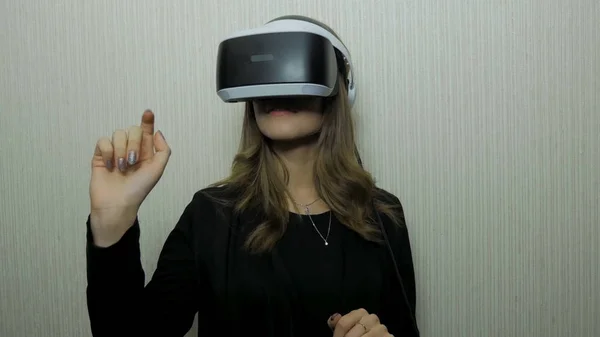 Mulher usando o dedo para tocar na visualização de painel imaginário no dispositivo VR contra a parede branca. Uso da menina do dispositivo do vr — Fotografia de Stock