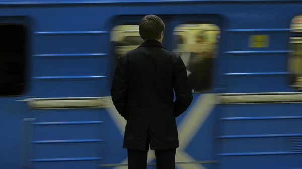 Die Rückansicht eines einsamen jungen Mannes, der an einer U-Bahn-Station von hinten erschossen wurde, fügt einen Blick auf die Uhr hinzu, die auf den Zug wartet. Geschäftsmann am Bahnhof — Stockfoto